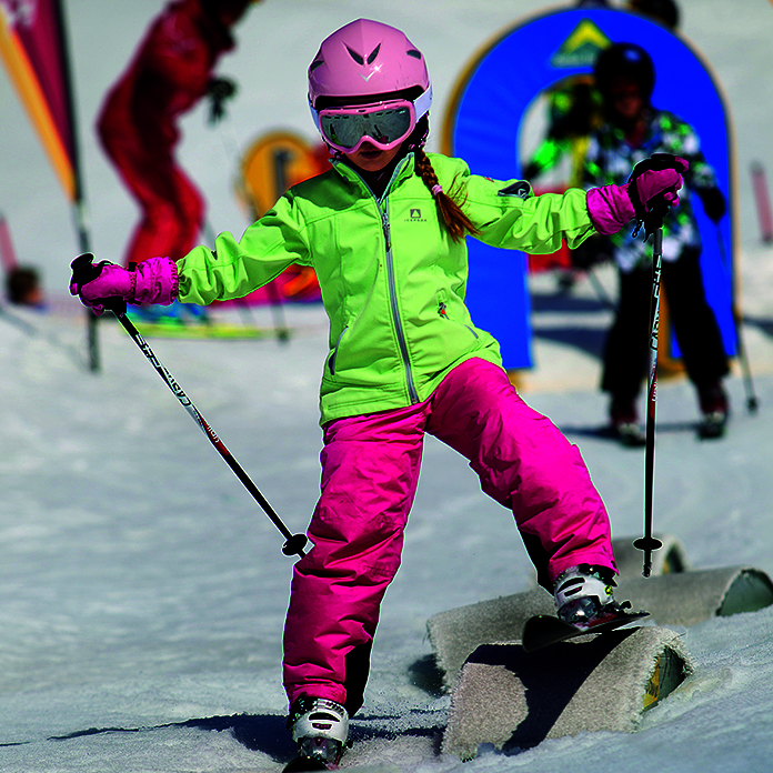Kind in pink-grünem Ski-Anzug und Skiern über Hindernissen