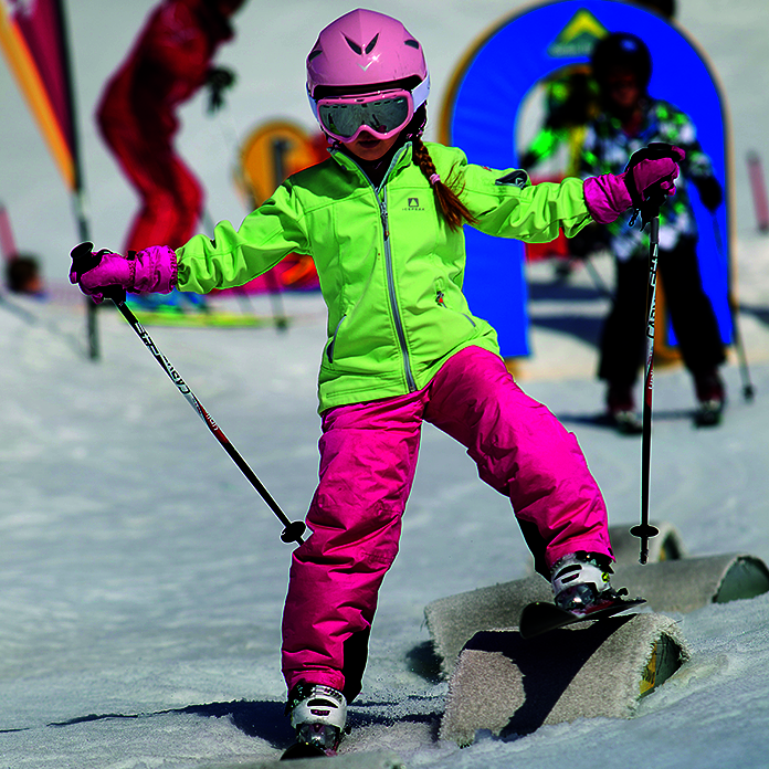 Kind in pink-grünem Ski-Anzug und Skiern über Hindernissen